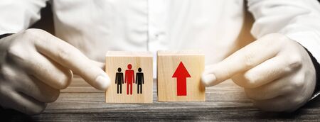 A man holds wooden blocks with the image of people and a red up arrow. The concept of population...