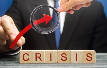 Businessman holds up arrow over blocks with the word Crisis. Increase instability of business and economy. Recession, stagnation, bankruptcy. Midlife crisis. Impoverishment. Debt and risk growthの写真素材