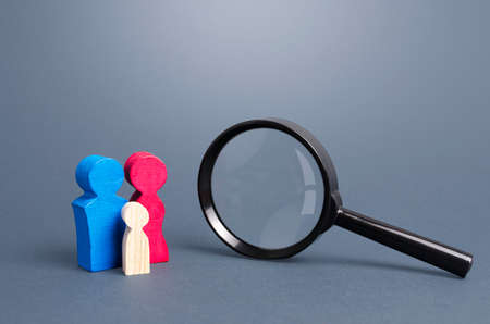 Figurines symbolizing the family and magnifying glass. Demographic policy. Gene research. Demographic studies, population. Search for couples to adopt orphaned children, integration into society.の写真素材