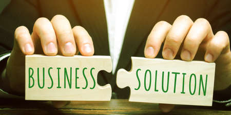 A businessman holds wooden puzzles with the words Business Solution. The concept of solving problems. Plan, planning. Analytics concept. Strategyの写真素材