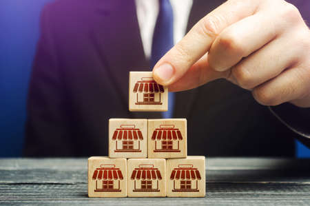 A man builds a pyramid from blocks of business shops. Building a successful business empire. Expansion and competitive growth. Franchise concession concept. Commercial network development.の写真素材