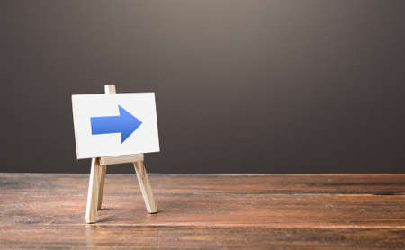 Easel with a blue right arrow. Sign of direction. Advertising of the location of a store or outlet. Restriction of movement, change of course. Short road. Minimalism. Distracting maneuver.の写真素材