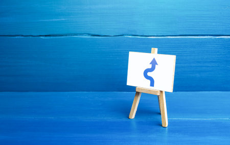 An easel with a curved arrow avoiding an obstacle. Deviation from route, side mission. Maneuvering, taking right action. Purposefulness and perseverance, confident movement towards the assigned goal.の写真素材