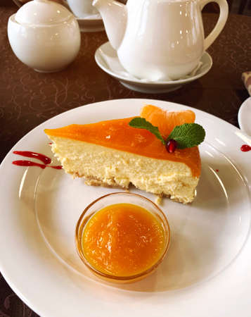 Tasty fruit cheesecake on a white plate with orange jam and a slice of mandarin. Sweet pastriesの写真素材