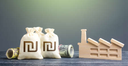 Israeli shekel money bags and industrial factory. Investments in production and energy industry. Subsidies support for businesses. Concession auction tender. Budget forming economy subjects.の写真素材