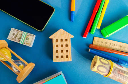 Miniature wooden house, money and hourglass on a blue background. Real estate concept. Affordable housing. Apartments for rent. Buying a house. Credit, loan, mortgage. Investmentsの写真素材