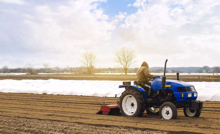 Farmer on a tractor with milling machine loosens, grinds and mixes soil. Loosening the surface, cultivating the land for further planting. Farming and agriculture. Cultivates the soil. Plows a field.の写真素材