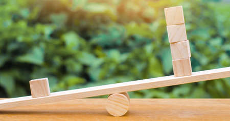 One wooden block on the scales outweighs the other four. Inequality concept. One against the others. Leadership and uniqueness. Unique, dissenting opinion, individual and standing out from the crowdの写真素材