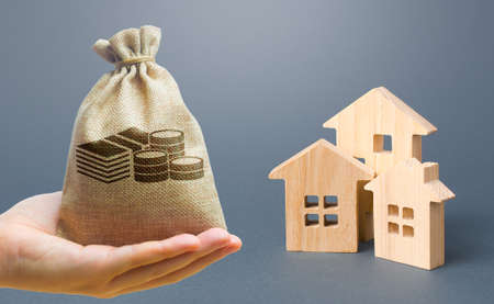 Money bag, wooden houses on a gray background. Buy purchase and sale of housing, rental. Community owners of apartments and houses. Construction industry, maintenance and utilities. Mortgageの写真素材