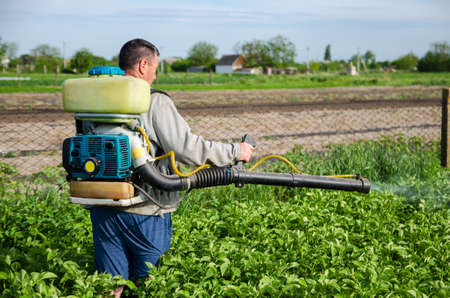 A farmer sprays chemicals on a potato plantation field. Control of use of chemicals growing food. Increased harvest. Protection of cultivated plants from insects and fungal infections.の写真素材