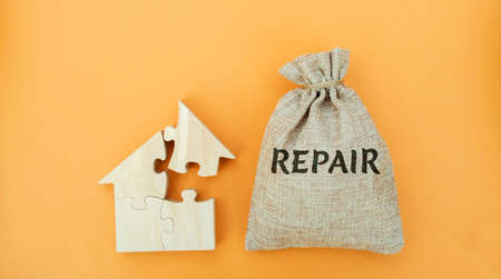 Money bag with the word Repair and a wooden house. The concept of a damaged house, dilapidated housing. Home repair after disaster. Renovation, restoration of the old building. Property maintenanceの写真素材