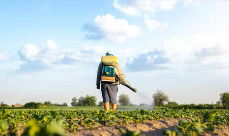 Farmer with a mist sprayer walks through farm field. Protection of cultivated plants from insects and fungal infections. Effective crop protection, environmental impactの写真素材