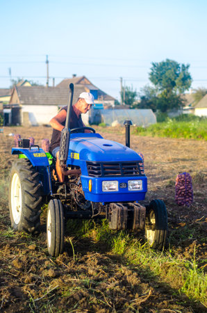 Kherson oblast, Ukraine - September 19, 2020: A farmer on a tractor with an aggregate of equipment for digging potato. Farming. Agricultural work in the field. Campaign harvesting potatoes in autumn.のeditorial素材