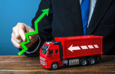 Businessman holds a green arrow up and a truck. Production growth. Import, export. End of containers shortage crisis. Transportation inflation, high shipping rates. Priced rise. Increase in traffic.の写真素材