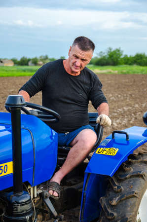 Kherson oblast, Ukraine - May 29, 2021: An elderly farmer sits and drives a tractor. Running a small agribusiness. Farming. Loosening, land cultivation. Mechanization in agriculture. Farm work.のeditorial素材