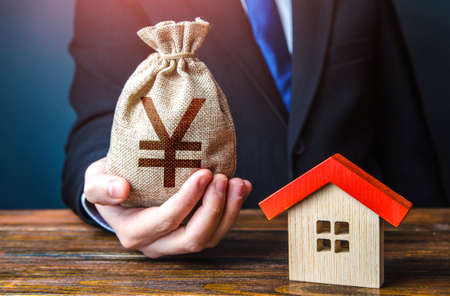 Man holds out a chinese yuan or japanese yen bag near the house. Home purchase, invest in real estate. Property appraisal. Favorable terms and conditions. Bank approval for issuing a mortgage loan.の写真素材