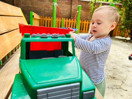 A little cute boy of one and a half years plays with toy car at the playground. Adorable toddler playing with cars and toys outdoor. Family, holiday, kids lifestyle concept. selective focusの写真素材