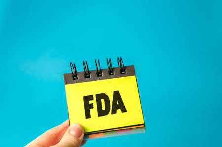 Sticky note in hands with the word FDA - Food and Drug Administration. Concept of promoting public...