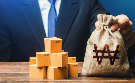 Businessman holds south korean won money bag and boxes with goods. import and export. business income. Payment of taxes and fees. advertising budget. Purchase and sale of goods, trade and commerce.の写真素材