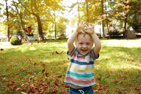 Happy toddler boy playing in the park with leaves on a sunny day. Smile boy of one and a half years...