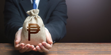 Businessman holds out philippine peso money bag. Getting a grant. Mortgage, loan approval. easy money. Salary benefits. Attracting investments. deposit savings. cashback. banking and crediting.の写真素材