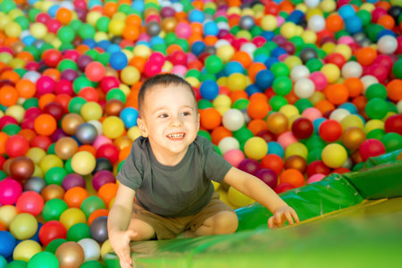 Happy smiling toddler boy climbs up on a slide in a children's room or children's entertainment center. Multi-colored balls. Happy active pastime and childhood. Playground. Selective focusの写真素材