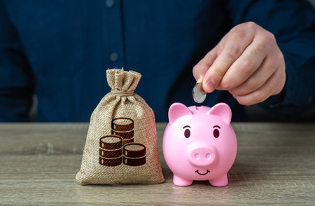 A man puts coins in a piggy bank. Accumulating money. Savings and investments. Collection of donations. Bank deposit. Raise funds for your dream. Reduce costs. Save for retirement.の写真素材