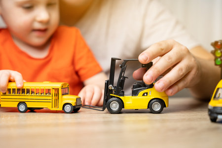 Father and son play with cars. Spending time with children. The concept of a happy childhood. School bus and forklift. Close up. Focus on the toy car.の写真素材