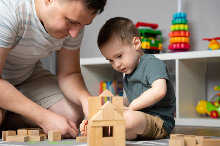 Little toddler boy 2.5 years playing wooden blocks with dad. Spending time with children. Educational activities for kids. Children's room. Indoors. Selective focusの写真素材