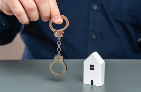A man holds handcuffs near his house. The concept of seizure of property for non-payment. Confiscation of real estate. Freezing of assets.の写真素材