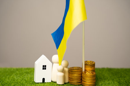 The concept of helping Ukrainian residents affected by the war. Financial support and donation. A family stands near a house, coins and the flag of Ukraine. Budgetの写真素材