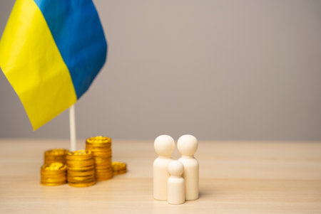 The concept of helping Ukrainian residents affected by the war. Financial support and donation. Economy, finance and fund. Family figures near the Ukrainian flag with coinsの写真素材