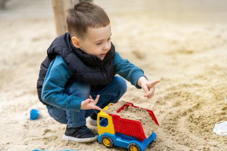 Little cute toddler boy three years old plays in the sandbox on a spring day. Outdoor development activities for kids. Toy carsの写真素材