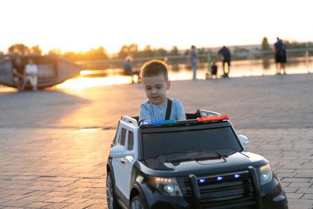 A little caucasian toddler boy of three and a half years old rides a toy car in a summer park near lake on a sunset light. Childhood and pastimeの写真素材