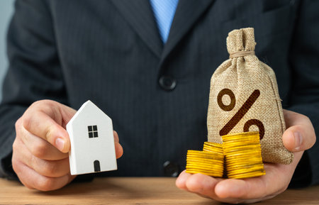 A man holds a money bag loan and a figurine of a white house. Buy a house in installments or with a mortgage loan. Investment in rental property. Buy housing.の写真素材