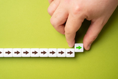 A hand makes a path out of blocks with arrows. The concept of moving forward and continuing progress. Strategic planning, forward momentum, and the continual pursuit of growth and improvementの写真素材