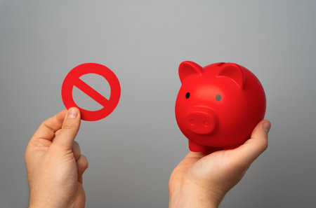 Red piggy bank and prohibitory sign no in hands on gray background. Overheated financial market. Difficult economic conditions. Heavy burden on budget. Financial restrictions and tighter regulation.の写真素材