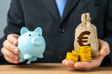 Businessman holds a piggy bank and a bag of money. Putting aside part of the profit for retirement or savings. Wealth management, investment strategies. Pension funds, financial stabilityの写真素材