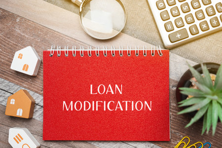 Loan modification concept - change made to the terms of an existing loan by a lender. Business and finance concept. Inscription on a notepad, miniature houses and a magnifying glassの写真素材
