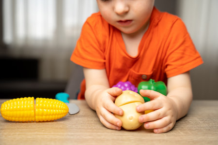A cute 3 year toddler boy plays with toy fruits or vegetables and sitting at the table. Velcro games. Selective focusの写真素材