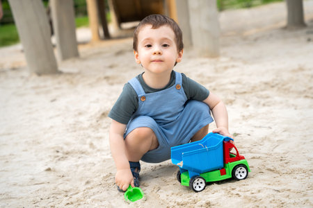 Little cute toddler boy 2.5 years old plays in the sandbox on a sunny summer day. Outdoor creative activities for kids. Toy car and shovel.の写真素材