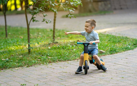 A cute smiling toddler boy of three or four years old rides a bicycle or balance bike in a city park on a sunny summer day. Toddlerhood and childhood concept. Selective focusの写真素材