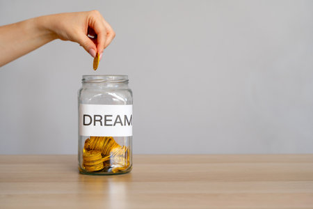 Savings money for a dream. Investments in the future. A woman's hand puts coins in a glass jar with money.の写真素材