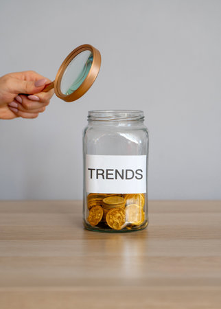 Bank of coins with the inscription Trends and magnifying glass. Analysis popular and relevant topics. New ideological trends of fashion. Recent and latest trend. Business and finance. Investmentsの写真素材