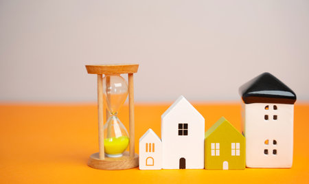 Miniature figures of houses and sand hourglass. Mortgage and loan concept. Temporary rental housing and residence permit. Time to pay taxes and bills. Realtor services for a quick search for options.の写真素材