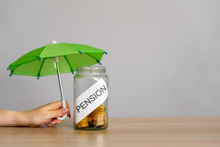 Bank of coins with the inscription Pension and green umbrella. Retirement Insurance concept. Financial support and regular payments to people after retirement. Business and financeの写真素材