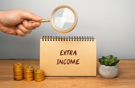 Extra income concept. Money earned in addition to a primary source of income, such as a salary or wages. notebook, magnifying glass and coinsの写真素材