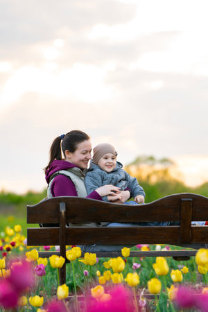 Happy mother and toddler hugging songing sitting on a bench along a field of tulips. Family spending time, lifestyle conceptの写真素材