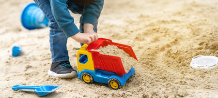 Little cute toddler boy three years old plays in the sandbox on a spring day. Outdoor development activities for kids. Toy cars and shovel. Focus on the carの写真素材