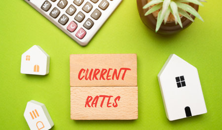 Current rates concept. Real estate mortgage interest rates. Buying and selling houses, apartments and housing. Inscription on wooden blocks and calculatorの写真素材